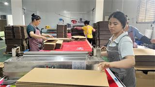 Workshop operator handling a paperboard sheet beside stacked material
