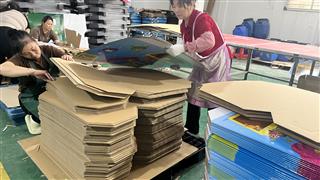 Staff handling board components beside printed display parts on a worktable
