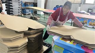 Workshop operator handling a shaped board panel beside stacked components
