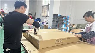 Workers handling a large shipping carton at a workshop packing table