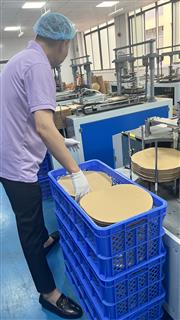 Operator beside a forming station with circular paper pieces in a blue crate