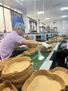 Workers handling formed air fryer paper liners along a Holidaypac production conveyor.