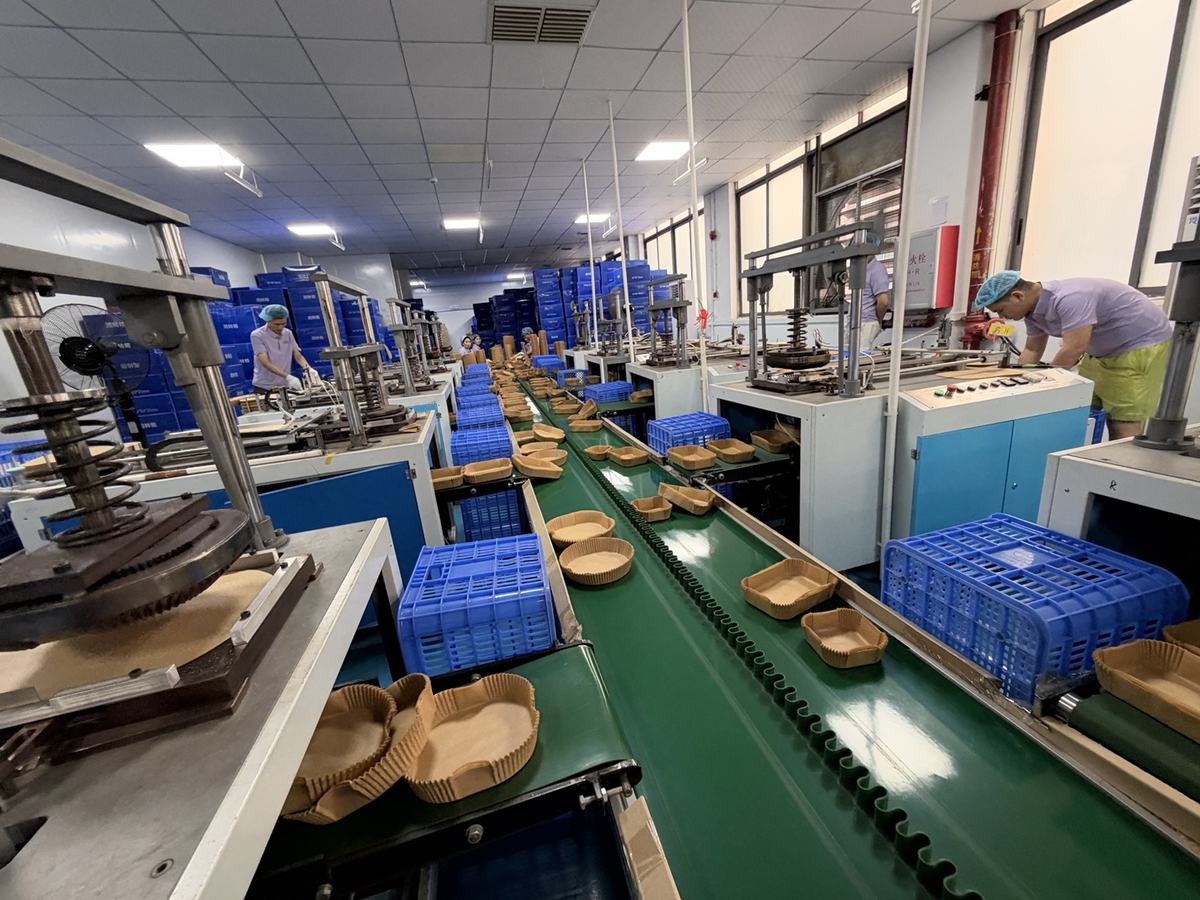 Holidaypac air fryer paper liner forming stations and paper trays moving along a workshop conveyor Holidaypac air fryer paper liner forming stations and paper trays moving along a workshop conveyor