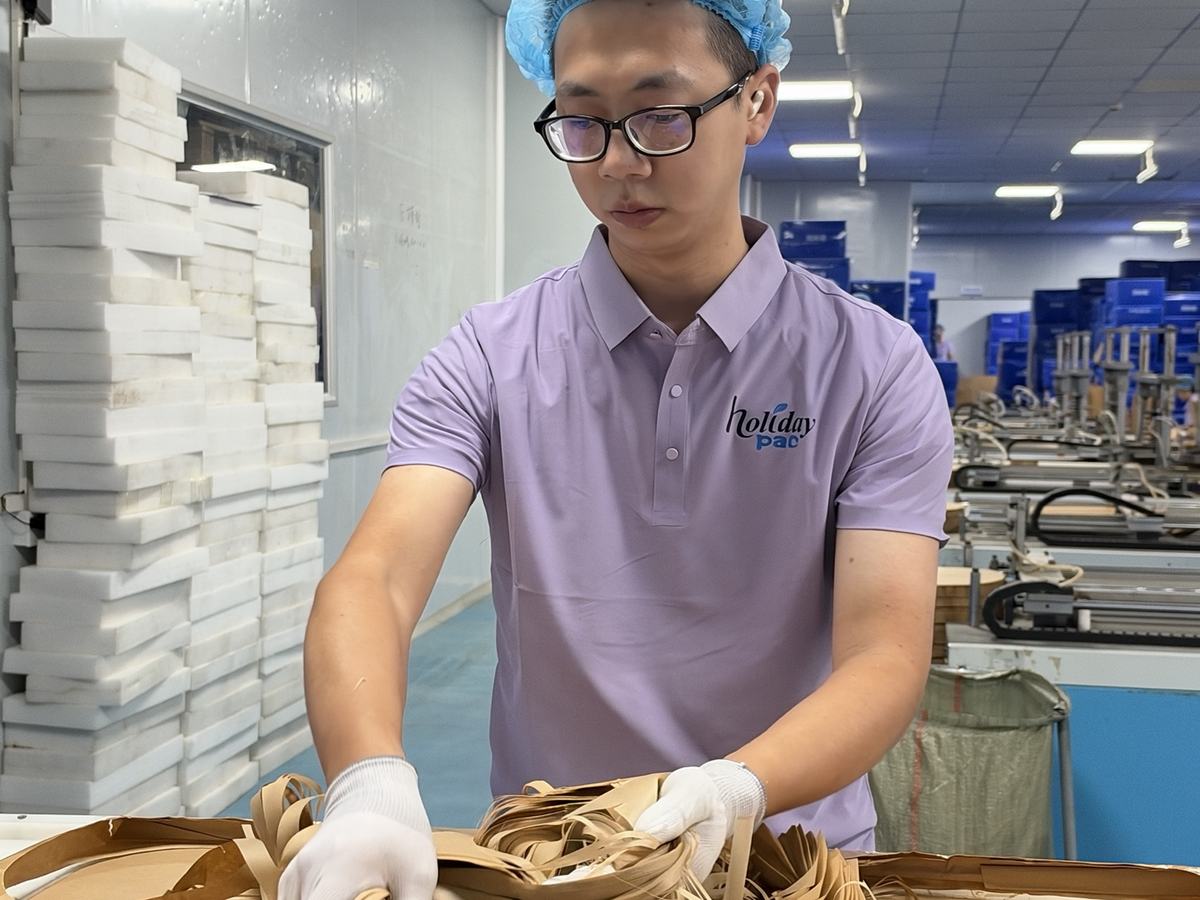 Holidaypac worker handling brown rectangular air fryer paper liner blanks at a packing table Holidaypac worker handling brown rectangular air fryer paper liner blanks at a packing table